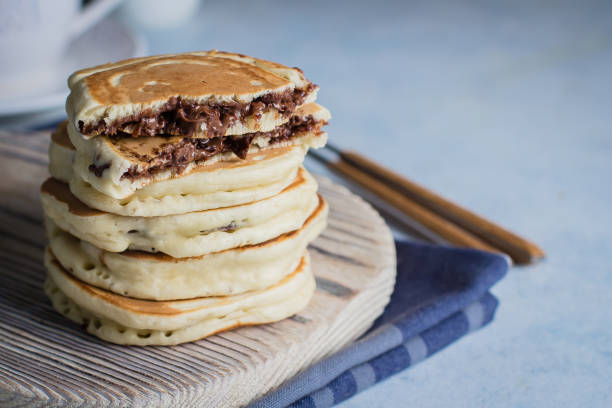 istock Stack of Stuffed chocolate nutella pancakes on vintage wooden board on blue table background with cup of tea. American Breakfast Concept. Copy space 922733696