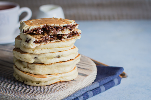 Stack of Stuffed chocolate nutella pancakes on vintage wooden board on blue table background with cup of tea. American Breakfast Concept. Copy space