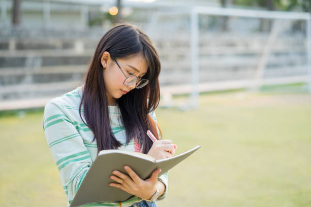 Teenage girl wearing eyeglasses standing write a notebook in football field at sunset stock photo