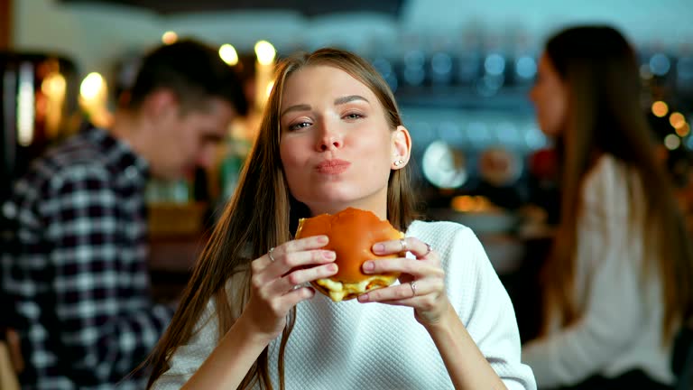 Young happy woman eating tasty fast food burger in cafe