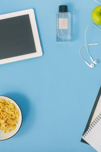 istock Flat lay home office desk. Feminine Workplace with tablet, notebook, perfumes, clipboard, headphones, wristwatch, apple and porridge on blue background, top view 922742396