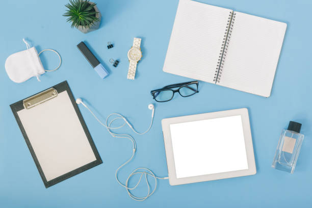 istock Home office workspace with  tablet, notebook, perfumes, spectacles, clipboard, headphones, wristwatch and felt-tip pen on blue background. Feminine Workplace concept. Flat lay, top view 922742516