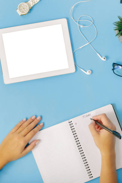 istock Feminine workplace flat lay, top view. Female hands write in notebook on blue background. Office desk workspace 922742518