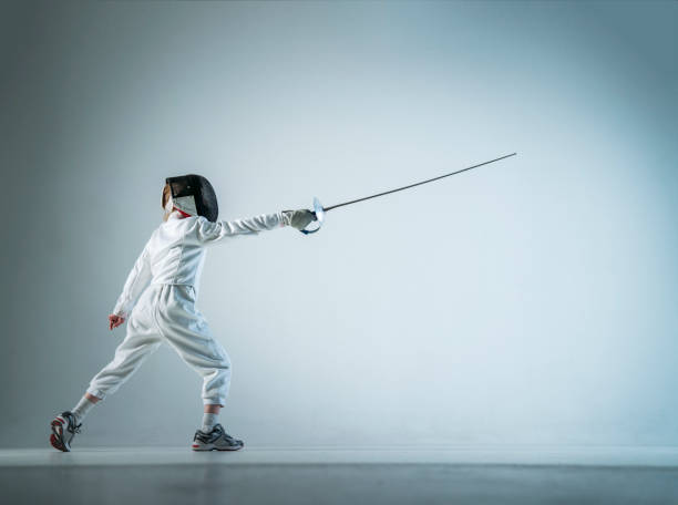 Boy fencing lunge over white background Full length of fencer standing in lunge position. Male athlete is with fencing foil practicing over white background. Boy is in sports clothing. fencing sport stock pictures, royalty-free photos & images