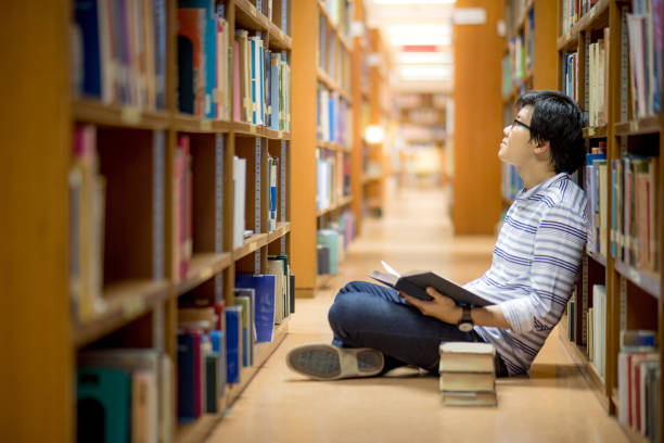 istock Young Asian man university student reading book in library 922750916