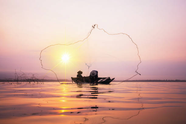 istock Fisherman on wooden boat casting a net. 922751088