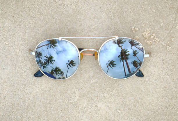 istock Mirrored sunglasses close up on the beach sand with palm trees reflection 922753230