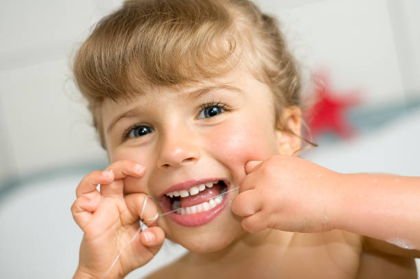 Cute girl cleaning teeth by floss in bathroom stock photo