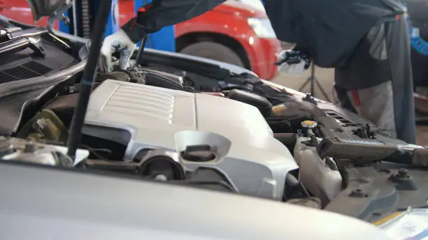 Mechanic in car garage checking hood of the luxury sportcar, horizontal