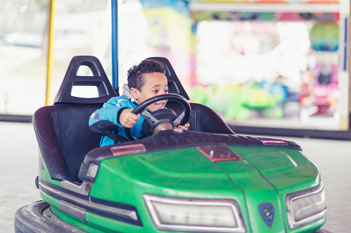 Mixed race boy driving bumper cars in amusement park