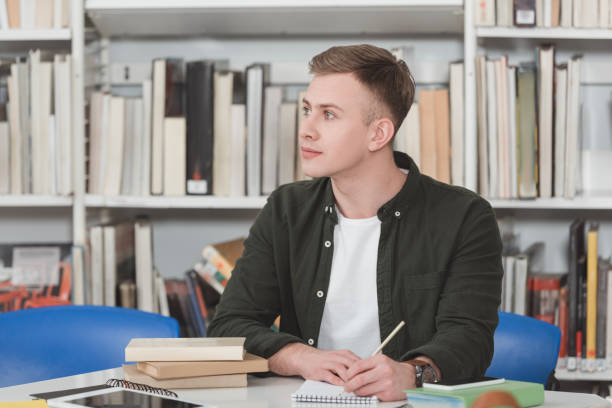 istock male student writing something to notebook and looking away in library 922772162