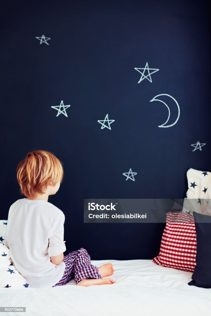 cute kid in pajamas dreaming , while sitting in bed and looking on chalkboard wall Bedroom Stock Photo