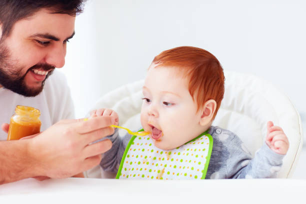 istock happy father feeding cute redhead baby with complementary food 922772820