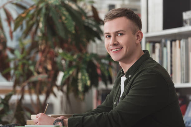 istock smiling male student sitting at table in library and looking at camera 922775418