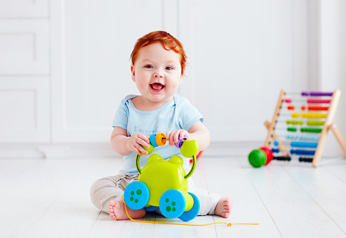 happy infant baby boy playing with toys at home