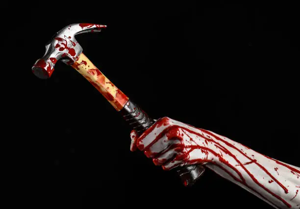 Photo of Bloody halloween theme: bloody hand holding a bloody hammer isolated on a black background