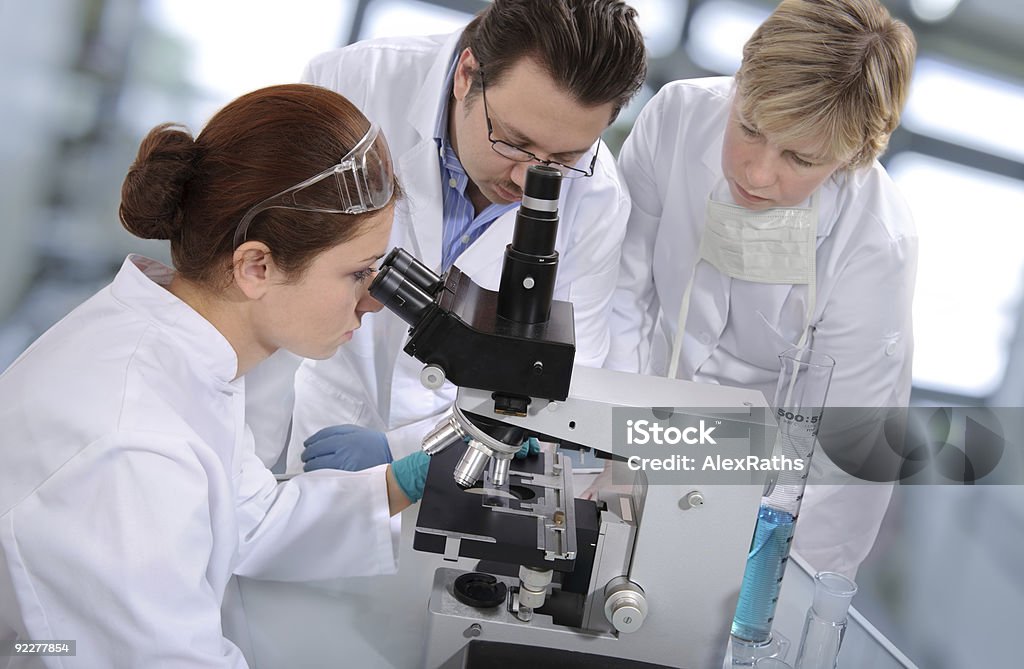 Group of scientist huddled around a microscope group of scientists working at the laboratory. Adult Stock Photo