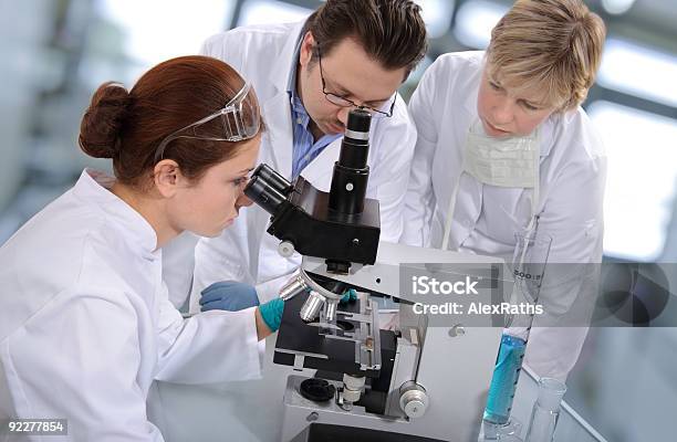 Group Of Scientist Huddled Around A Microscope Stock Photo - Download Image Now - Adult, Beaker, Biology