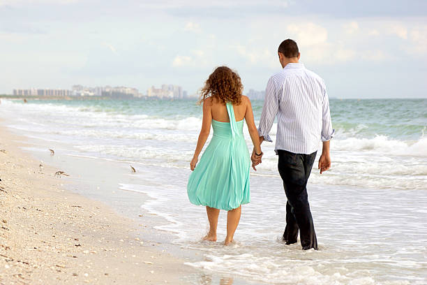 Happy senior man and woman couple dancing and holding hands on a deserted tropical beach with bright clear blue sky