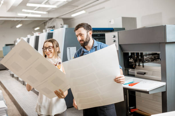 Woman with print operator at the printing manufacturing Young woman designer and print operator working with paper print at the print manufacturing with offset machine on the background manufacturing occupation photos stock pictures, royalty-free photos & images