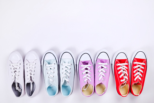 International womens day sale clearance. Variety row of different colorful casual shoes on white background. Spring-summer collection. White, blue, purple, red low top sneakers. Copy space, top view.