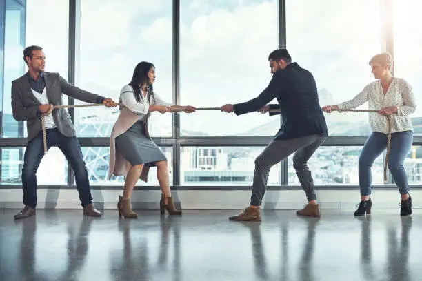 Shot of a group of businesspeople pulling on a rope during tug of war in an office