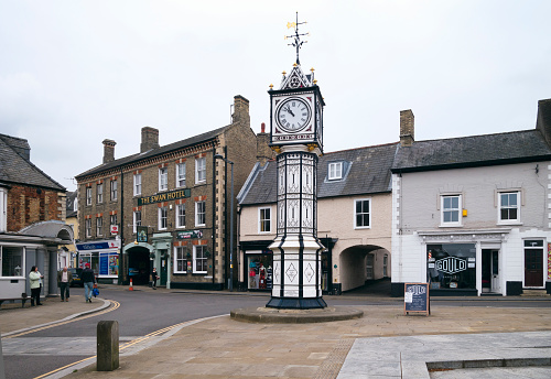 A few people walking near the clock tower in the centre of Downham Market in Norfolk, eastern England. Downham Market is typical small market town, with a mixture of shops and other facilities and has a population of around 10,000. The clock tower was constructed in 1878.