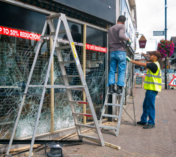 Two workmen repairing the vandalised window of a jewellery shop which was broken during the riots in England 2011, following the death of Mark Duggan. The shop was in Beckenham, Kent (Greater London).