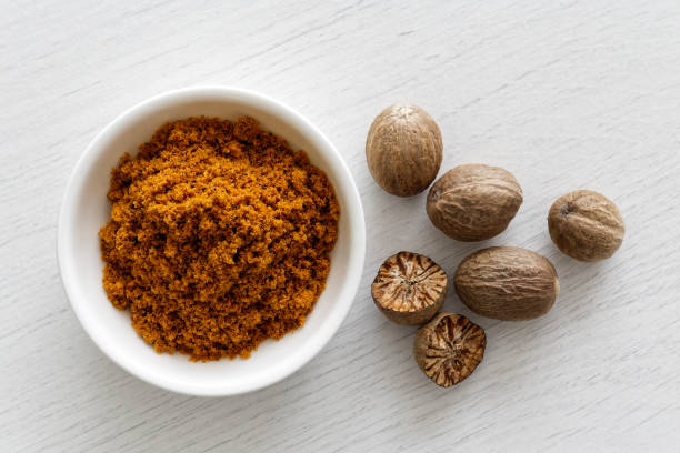 Ground dry mace in white ceramic bowl isolated on white wood background from above. Whole and halved nutmegs. Ground dry mace in white ceramic bowl isolated on white wood background from above. Whole and halved nutmegs. mace spice stock pictures, royalty-free photos & images