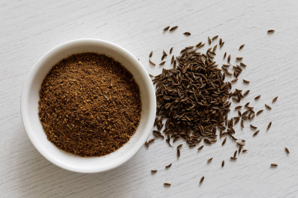 Ground cumin in white ceramic bowl isolated on white wood background from above. Whole cumin. Ground cumin in white ceramic bowl isolated on white wood background from above. Whole cumin. cumin stock pictures, royalty-free photos & images