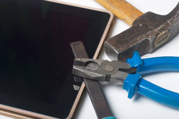 istock Tablet and working tools. On the white surface of the table is a tablet, skein, chisel and pliers. Destruction and repair of electronic devices. 922798808