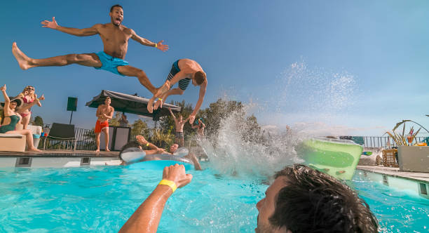 istock Two men jumping into pool and splashing water on their friends 922799002