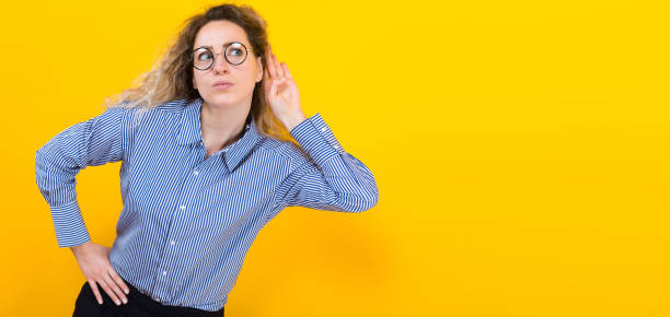Woman listening to something Portrait of curly-haired woman in striped shirt isolated on orange background trying hard to secretly listen to conversation hand to ear interested at gossip she hears privacy violation concept. social listening stock pictures, royalty-free photos & images
