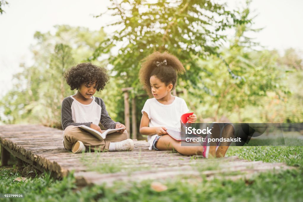 kids reading book little Afro child girl reading book between green spikes meadow garden with friend  read education concept Reading Stock Photo