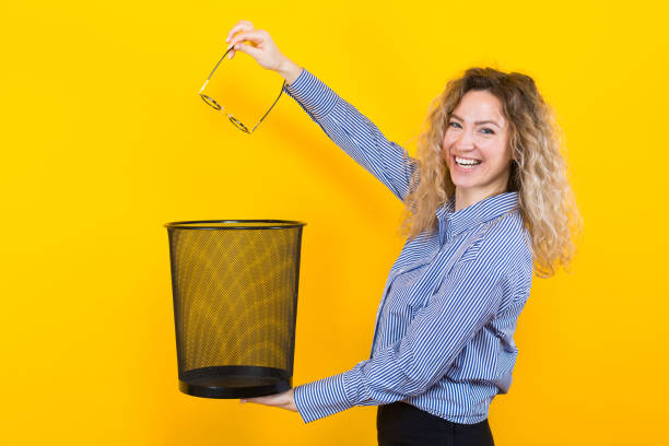 Woman throw away her glasses Portrait of curly-haired woman in striped shirt isolated on orange background throwing glasses she doesn't need any more into trash bin surgical correction of eyesight concept. myopia photos stock pictures, royalty-free photos & images