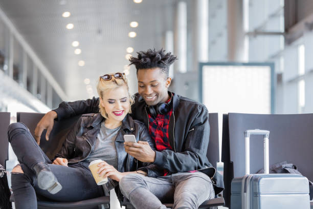 istock Young funky couple using mobile phone in airport lounge 922803620