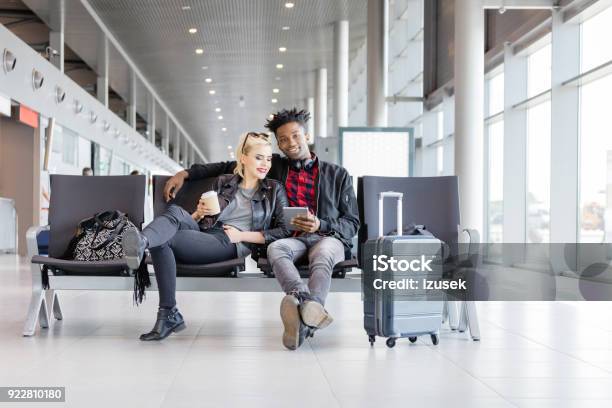 Multi Ethnic Funky Couple Waiting For Flight In Airport Lounge Stock Photo - Download Image Now