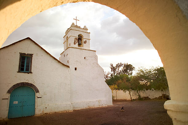 A traditional church located in the Atacama Desert, Chile, featuring rustic architecture and a prominent Chilean flag against a clear blue sky.