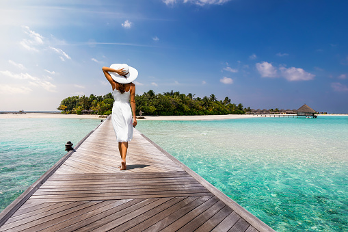 Attractive woman in white walks over a wooden jetty towards a tropical island