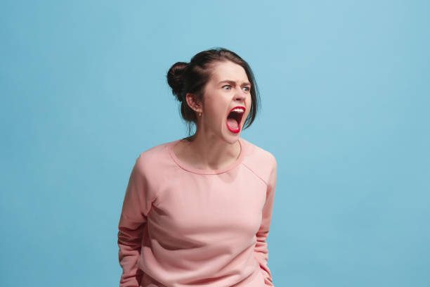 la joven enojada emocional gritando sobre fondo azul estudio - aggression fotografías e imágenes de stock