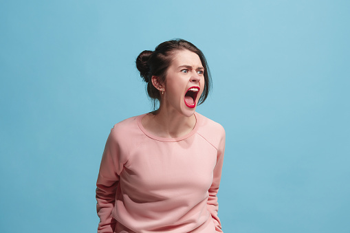 Screaming, hate, rage. Crying emotional angry woman screaming on blue studio background. Emotional, young face. Female half-length portrait. Human emotions, facial expression concept. Trendy colors