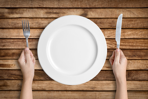 Dinner place setting. A white plate with silver fork and knife isolated on wood background with clipping path