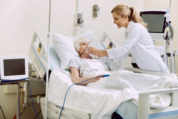 Smiling physician adjusting respiratory support at hospital DO not worry. Friendly female medical worker smiling while helping her retired patient and adjusting an oxygen mask at hospital. oxygen monitor stock pictures, royalty-free photos & images