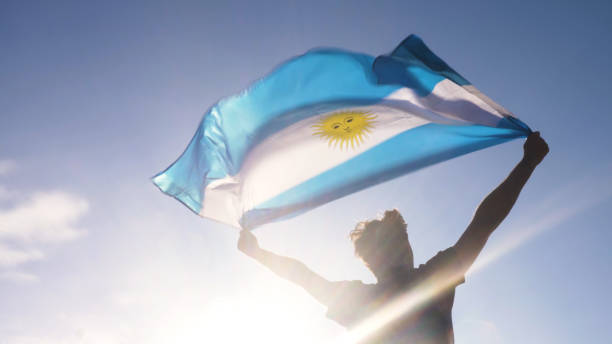 young man holding argentinian national flag to the sky with two hands at the beach at sunset argentina - argentina imagens e fotografias de stock