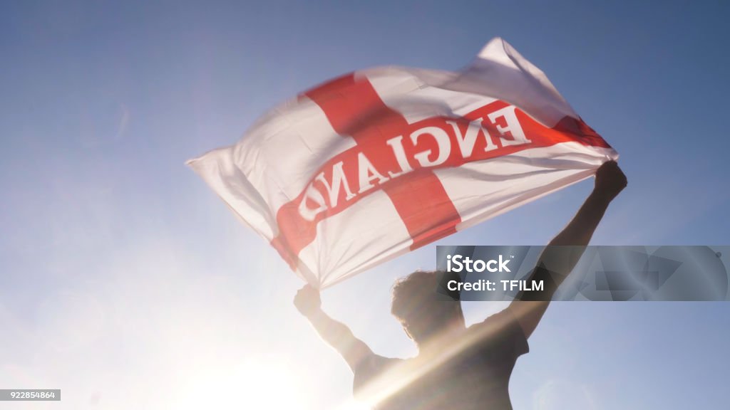 Young man holding england national flag to the sky with two hands at the beach at sunset uk united kingdom Young man holding england national flag to the sky with two hands at the beach at sunset Soccer Stock Photo