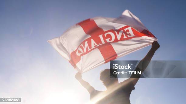 Young Man Holding England National Flag To The Sky With Two Hands At The Beach At Sunset Uk United Kingdom Stock Photo - Download Image Now