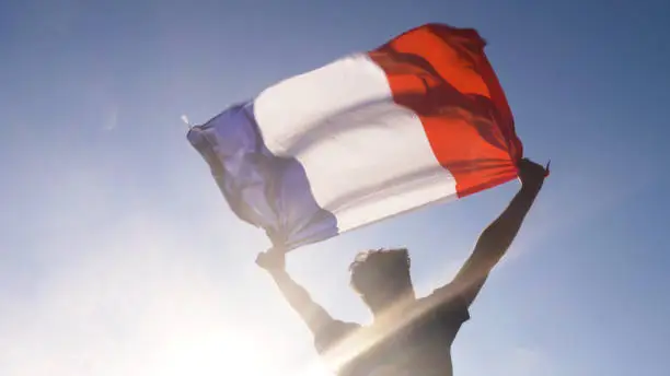 Photo of Young man holding french national flag to the sky with two hands at the beach at sunset france