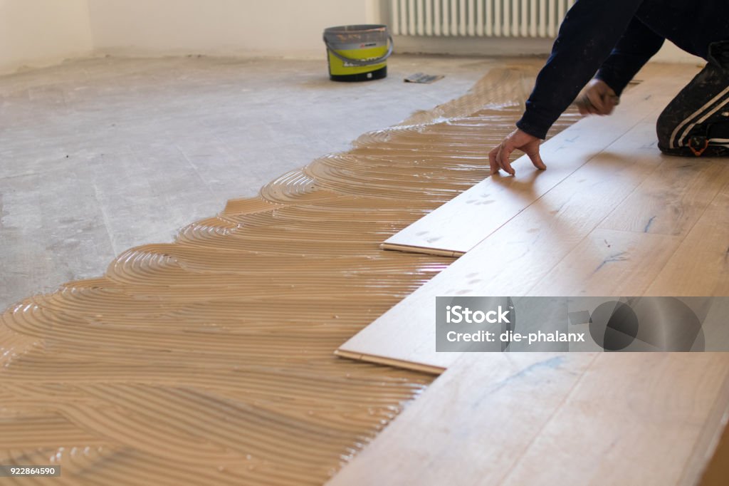 Renovation of an apartment, skilled worker uses a plastic hammer when installing pre-finished interlocking parquet. Renovation of an apartment, skilled worker uses a plastic hammer when installing pre-finished interlocking parquet. Laying with brown glue on an existing floor. Installation of oak colored parquet Flooring Stock Photo