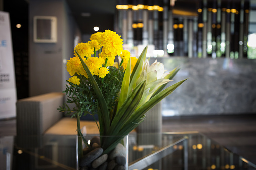 a glass vase of marigold put on the table in lobby of building
