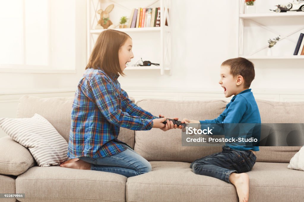 Siblings fighting over remote control at home Siblings fighting over remote control at home, brother and sister have quarrel, copy space Arguing Stock Photo